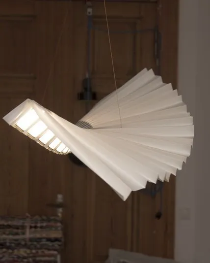 Gefaltete Origami-Leuchte Beo schwebt vor einer Holztür