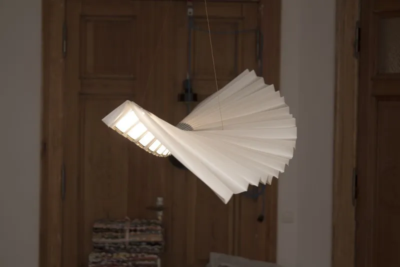 Gefaltete Origami-Leuchte Beo schwebt vor einer Holztür