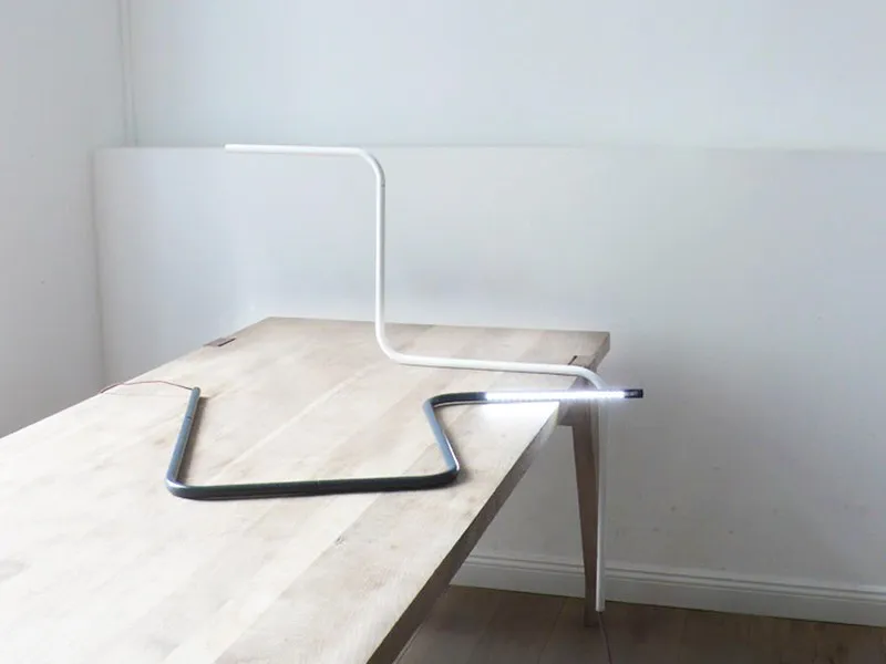 Linus Leuchte als gebogenes Rohr auf einem Holztisch