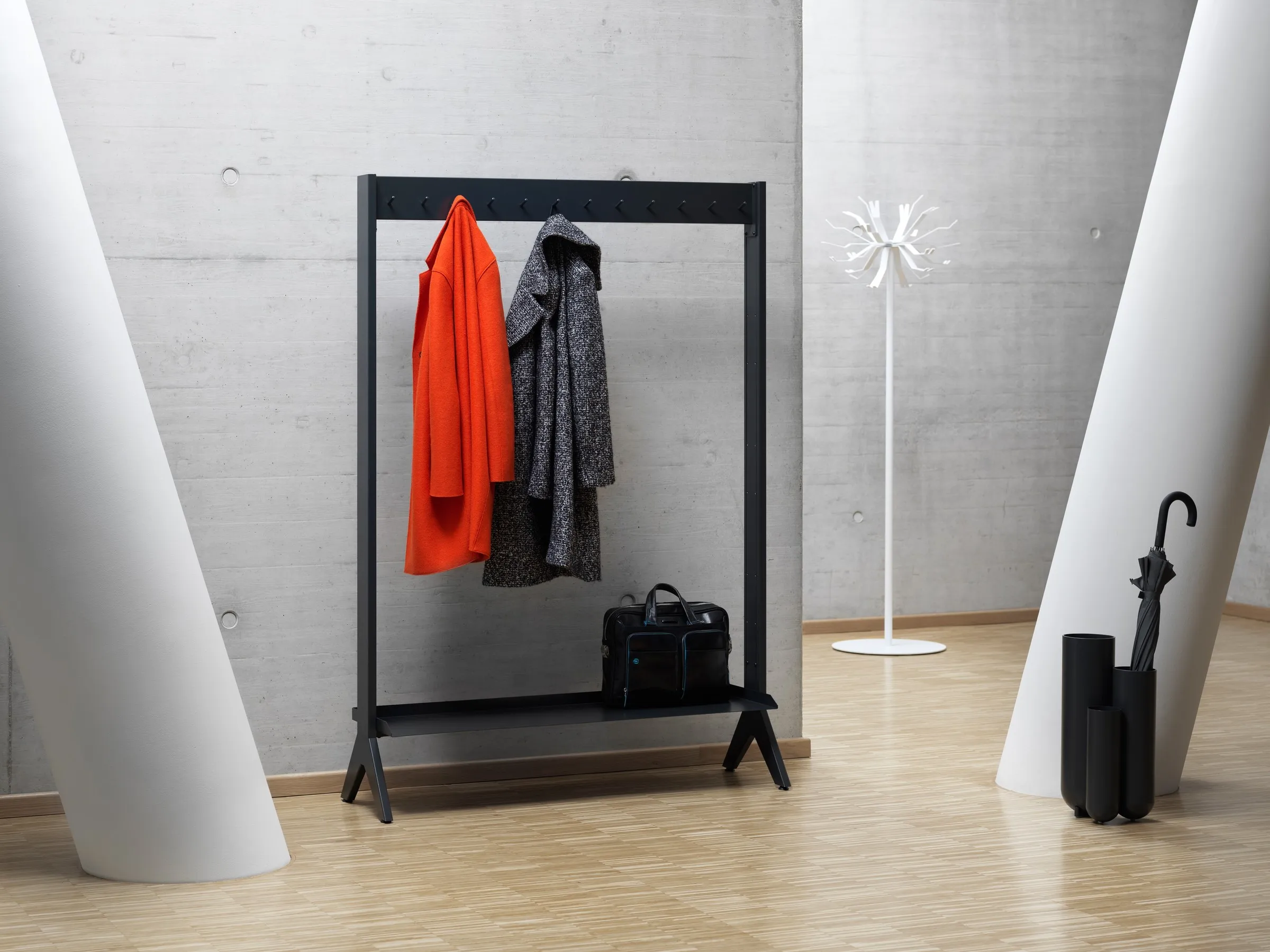 Schwarze SCALA Garderobe mit rotem Mantel vor Betonwand und Säulen