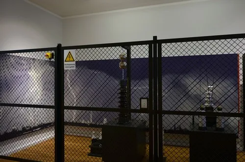 Hochspannungsexponat hinter Gitter vor großflächiger Blitzgrafik an der Wand