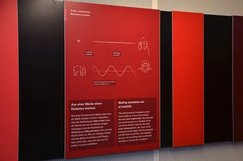 Rote Wandtafel mit Infografik zu Schallwellen zwischen schwarzen Paneelen