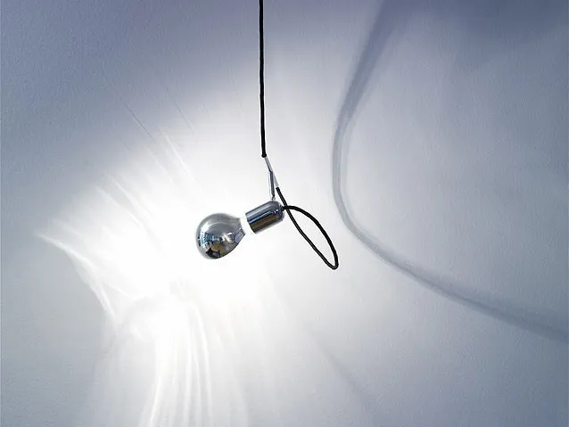 re-flect Leuchte hängt an schwarzem Kabel und strahlt gegen eine Wand